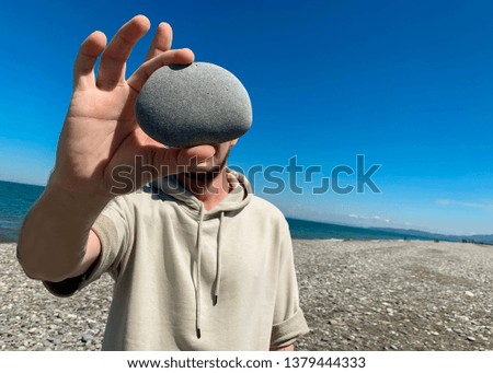 man holds a stone in front of his face. A place for a label