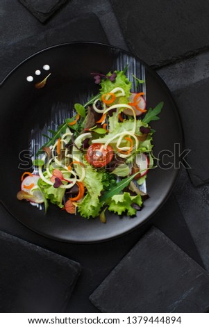 Green salad with microgreens on a black plate top view