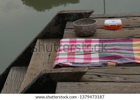 Loincloth , bathing cloth,vintage aluminum bowl and soap box on old wooden bridge beside stair.All items for Thai people to take the bath in canal.Selective focused and background is canal.
