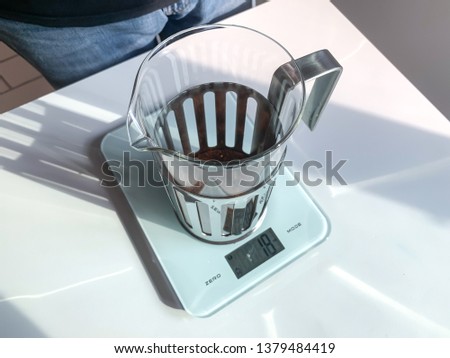 French press coffee maker is on the scale calculator on the white table.