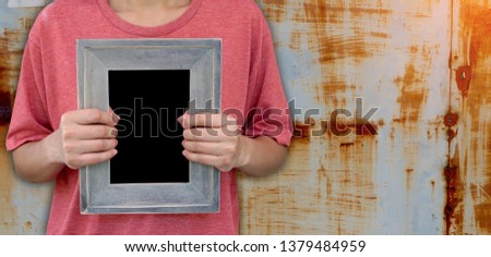 Female in a pink t-shirt caught in an empty hand, a vertical wooden picture frame that is empty on a dirty background. Space for pictures, letters, design or logo. Concept: Feelings are not beautiful.