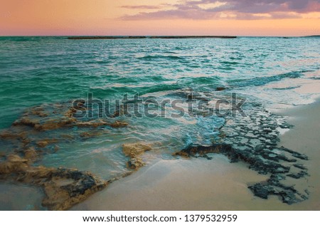 View of empty sandy Poseidon Beach near ayia napa, Cyrpus. Sunset, orange and purple sky among gray clouds above dark blue rippled water, shallow water with reefs. Warm evening in fall. Copy space