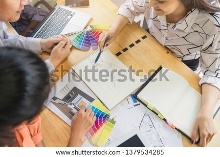 Architect designer Interior creative working hand drawing sketch plan and selection material color.  Young designers are using a laptop, discussing ideas and smiling while working in office.