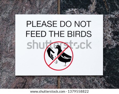 Black and white sign on stone wall with text PLEASE DO NOT FEED THE BIRDS and picture of bird and hand with food inside red crossed circle