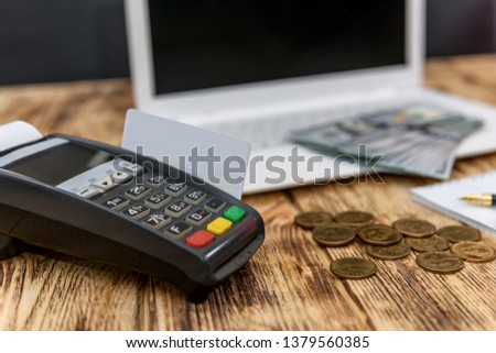 Banking terminal with dollar coins and laptop behind