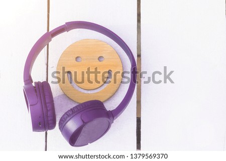 Fine music for perfect mood. Wireless purple headphones and a wooden smile on a white background. New technologies. Modern technology. copyspace