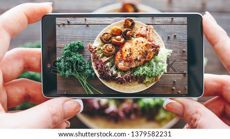 Culinary blog. Home cooking hobby. Food recipe. Closeup of female hands taking picture of roasted meat with grilled mushrooms.
