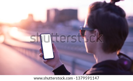 Woman holding smartphone with blank screen at sunset.