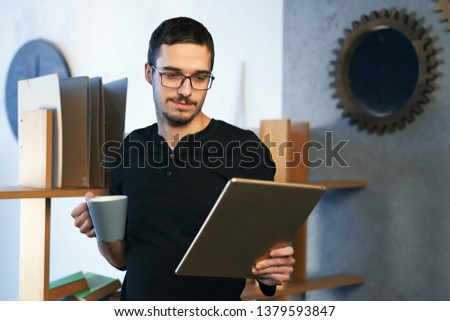 Young man working with computer, phone and tablet at the table while drinking coffee