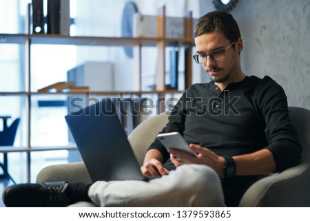 Young man working with computer, phone and tablet at the table while drinking coffee
