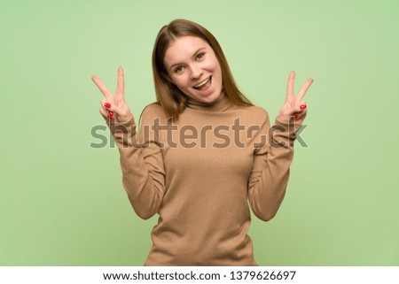 Young woman with turtleneck sweater showing victory sign with both hands
