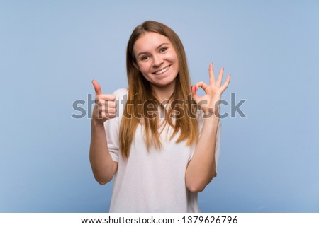 Young woman over blue wall showing ok sign with and giving a thumb up gesture