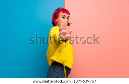 Young woman with yellow jacket making stop gesture for disappointed with an opinion
