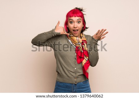 Young woman with pink hair over yellow wall making phone gesture and doubting