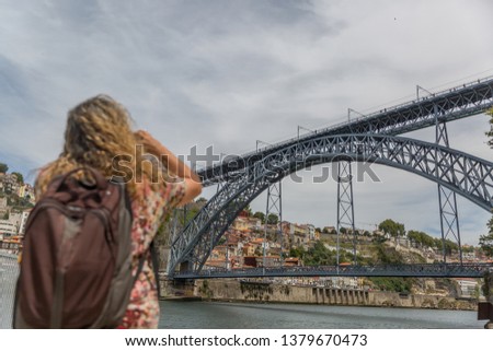 A mature tourist woman with a large backpack on her back, takes a photo of the famous Don Luis I Bridge in the city of Porto, Portugal
