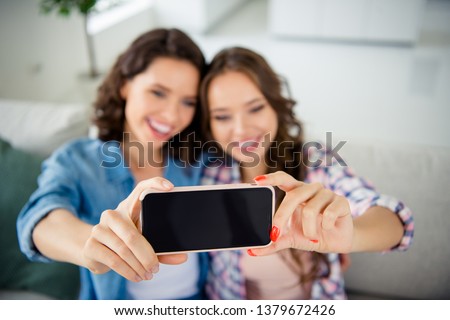 Close up photo beautiful she her cute ladies buddies make take selfies blurry focus arms hands telephone wear casual jeans denim checkered plaid shirts apartments sit comfy divan couch room indoors