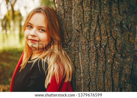 pretty cute girl with make up, dressed in black dress standing in a autumn park near tree