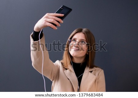young beautiful girl in glasses on a dark background listens to music, takes a selfie and smiles