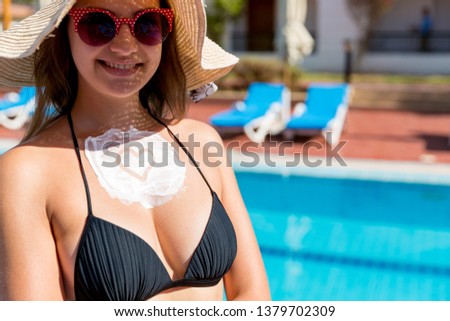 Beautiful woman with sun cream in heart shape on her breast by the pool. Sun Protection Factor in vacation, concept.