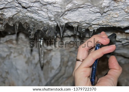 female hand uses a smartphone to take pictures of icicles on the ceiling of the cave