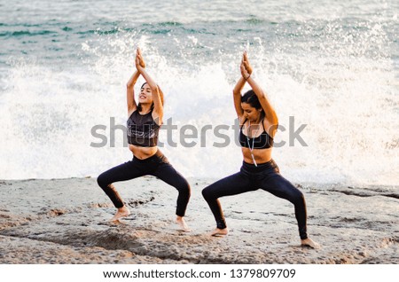 Woman yogi in a dark suit practicing yoga concept, standing in the exercise of Sumo Squat, Goddess pose, working, beach background with waves
