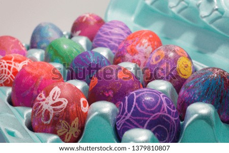 From within an egg carton, more than a dozen Easter eggs showcase their beautifully colored shells, decorated with wax crayons and soaked in dye to produce layers of deep, bright colors and designs.