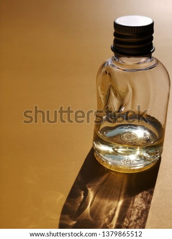 Slightly crumpled plastic bottle or jar with transparent liquid, presumably shampoo. Abstract close-up backlit photo of packaging design on brown or dark golden color background with space for text. 