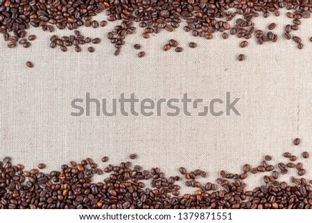 Roasted coffee beans arranged on top and bottom sides of linea canvas leaving an open space in middle, shot from above.