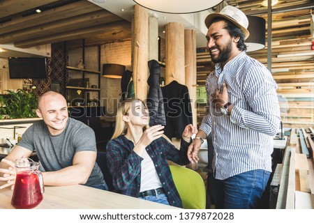 a group of young cheerful friends are sitting in a cafe, eating, drinking drinks, take selfies and take pictures. meeting, handshake and hugs