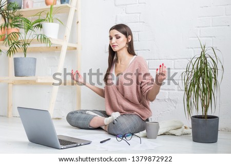 A young happy woman sits on the floor in a bright apartment or office interior and works at a laptop, freelancer girl at work, the concept of distance learning students, paperwork and online learning