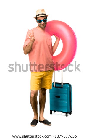 A full-length shot of Man with hat and sunglasses on his summer vacation happy and counting three with fingers on isolated background