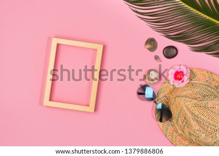 Stylish summer composition with photo frame, green leaves, hat and sunglasses on a pink pastel background. Artwork mockup with copy space