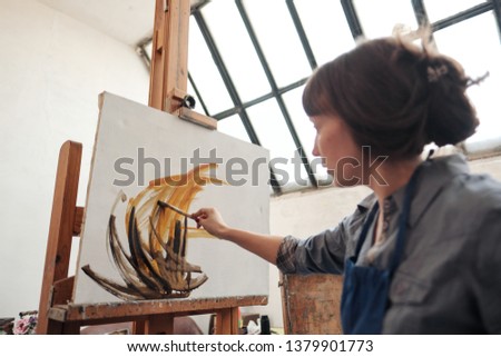 Young beautiful woman painter among easels and canvases in a bright studio. Inspiration and hobby.