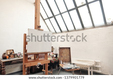 Bright art studio with a large window. Easels and canvases, workplace.