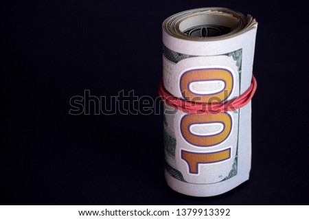 Twisted dollar bills in roll on dark background.
