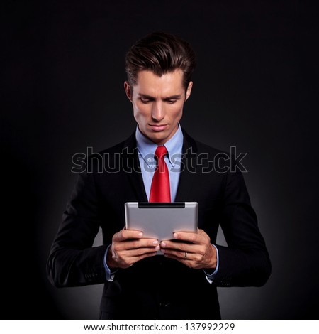 portrait of a young business man standing against a black background, holding and looking at a tablet