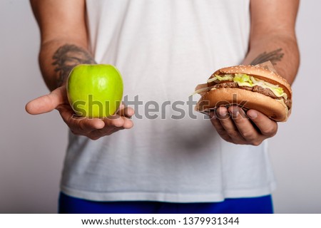 concept man makes the choice between healthy and unhealthy food. the choice between a burger and an apple. will power when dieting. fat man on an isolated background