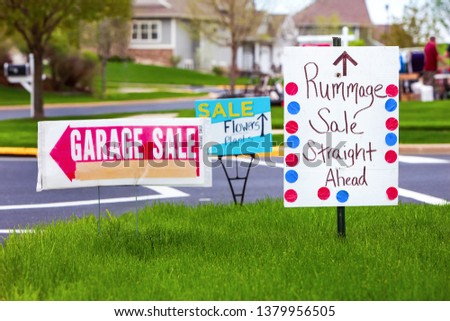 Garage sale signs on the lawn of a suburban home, main focus on white sign with dots