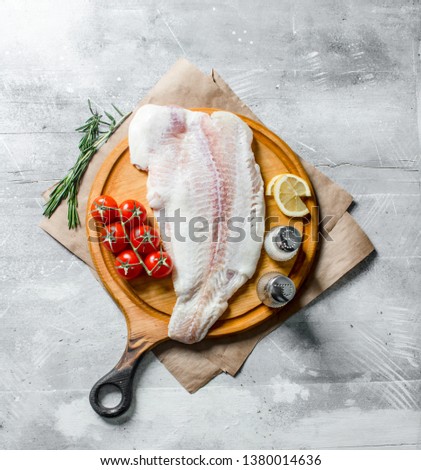 Fish fillet on cutting Board with rosemary, tomatoes, lemon slices and spices. On white rustic background