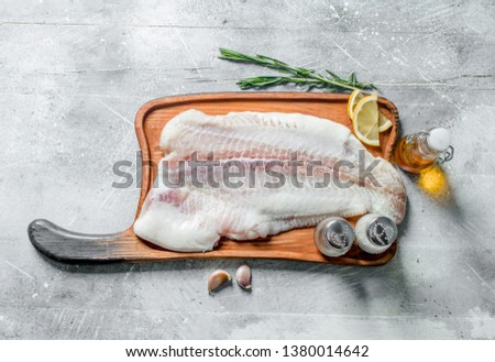 Fish fillet on a cutting Board with rosemary, spices, lemon slices and oil. On rustic background