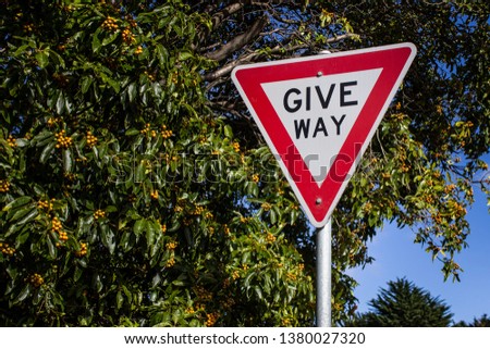 Give Way road sign against blue sky and green bushes