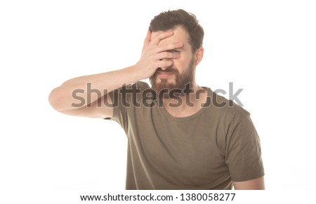 Portrait of a scared man covering his face with palm and looking at camera through fingers isolated on a white background 