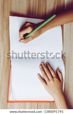 Close shot of a human hand writing something on the paper on the table