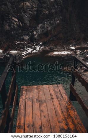 wooden observation deck above the river in the mountains with swirling stream of water. Big boulders in mountain creek background. Bukovel, Ukraine in winter season 