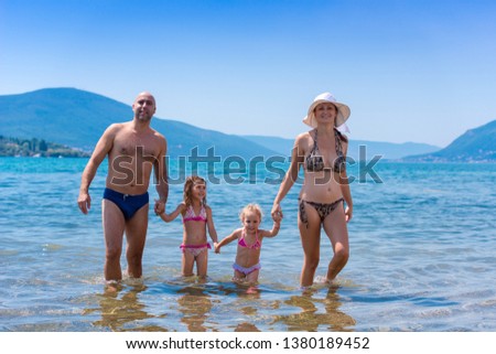 portrait of a young happy couple with cute little daughters having fun while standing in the shallow water of the sea during Summer vacation  Healthy family holiday concept