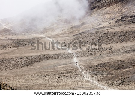 Thin road in a mountains leads to the top. Sand and stones on the ground, dry land. Clouds up on the sky. Travelling in a desert of Africa. Sunny hot day for outdoor trip.