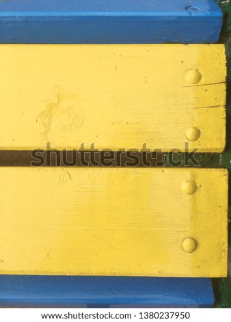 Background yellow and blue wood texture, photo for text new texture unusual on a city street. A fragment of a wooden bench on the bolt ah iron new painted.