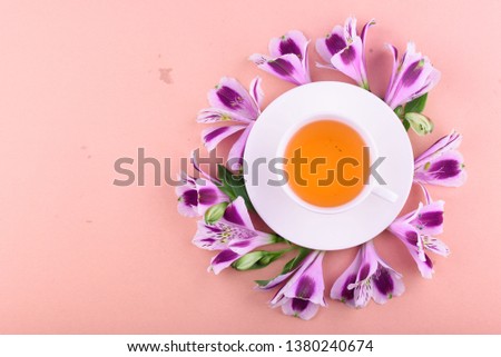 Fragrant tea in a white cup with beautiful flowers on a pink background