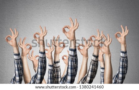 Row of man hands showing okay gesture. Agreement and approval group of signs. Human hands gesturing on background of grey wall. Many arms raised together and present popular gesture.