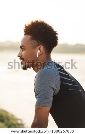 Picture of a handsome young african strong sports man listening music with earphones outdoors.